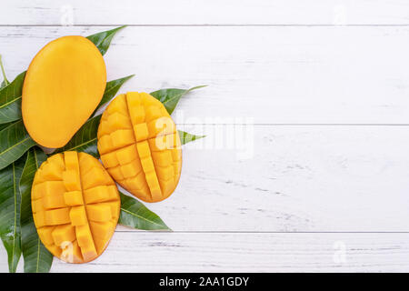 Bella trito di mango maturo con foglie di colore verde su bianco luminoso con il colore di sfondo di legno, vista dall'alto, laici piana, copia dello spazio. La frutta tropicale di design. Foto Stock