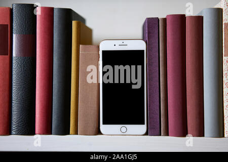 Telefono cellulare tra libri colorati in un ripiano Foto Stock