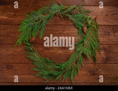 Composizione di natale. Ghirlanda fatta di albero di natale rami, sul legno scuro dello sfondo. Natale, concetto d'inverno. Appartamento laico, vista dall'alto. Foto Stock