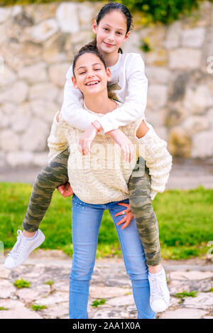 Due giovani ragazze a giocare un gioco insieme alla giornata di sole. Migliori amici divertendosi in estate a cavallo tra di loro con la schiena. Sorelle adolescenti su un parco cittadino in estate. Foto Stock