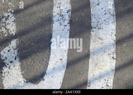 Primo piano della superficie di asfalto con vernice bianca e ombra da recinzione su di esso. Sfondo astratto Foto Stock