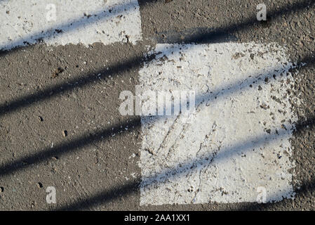 Primo piano della superficie di asfalto con vernice bianca e ombra da recinzione su di esso. Sfondo astratto Foto Stock