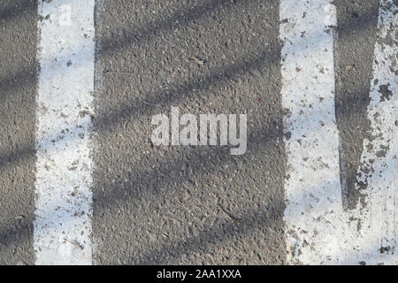 Primo piano della superficie di asfalto con vernice bianca e ombra da recinzione su di esso. Sfondo astratto Foto Stock