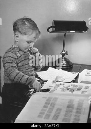 Hobby negli anni cinquanta. Un ragazzo è seduto a tavola con la sua collezione di francobolli. Egli ha una speciale album in cui egli li tiene in qualche tipo di ordine per bambini. La Svezia degli anni cinquanta Foto Stock