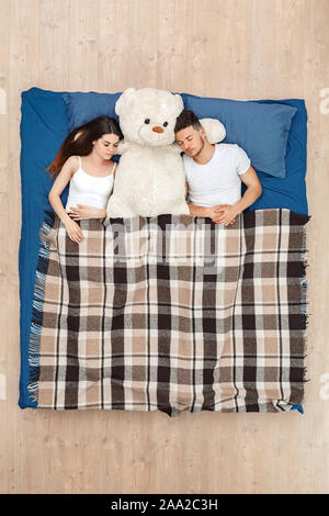Andare a dormire. Coppia giovane che dorme sul letto vista superiore sotto coperta con Teddy carino Foto Stock