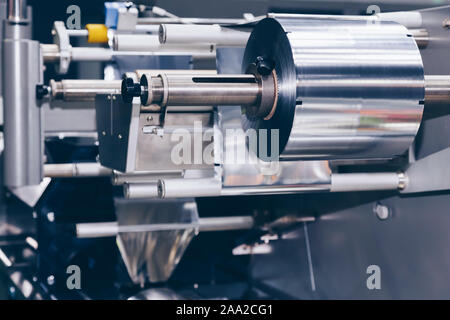 Rotolo di lamina di alluminio per il confezionamento di alimenti sulla macchina impacchettatrice automatica nel prodotto alimentare fabbrica. industriale e concetto tecnologico. Foto Stock