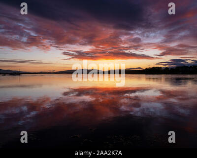 Rosso infuocato, rosa, viola e arancione tramonto riflesso nella calma, ancora la presenza di acqua in corrispondenza della bocca del Loch Etive, Connel, Oban, Argyll and Bute, Scotland, Regno Unito Foto Stock