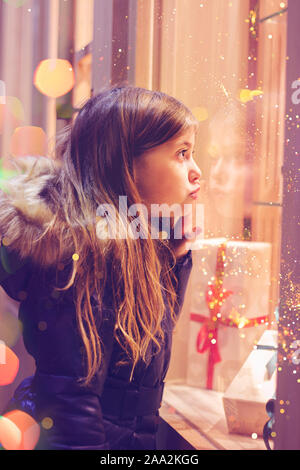 Bellissima bambina nella parte anteriore del negozio di dolciumi, decorata con avvolto confezioni regalo e caramelle. Concetto di natale, window shopping Foto Stock