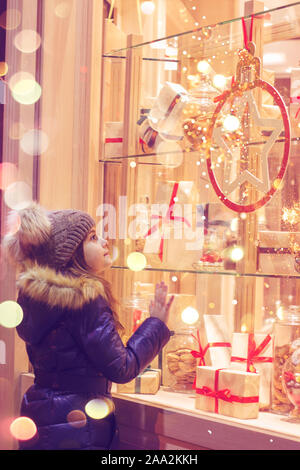 Bellissima bambina nella parte anteriore del negozio di dolciumi, decorata con avvolto confezioni regalo e caramelle. Concetto di natale, window shopping Foto Stock