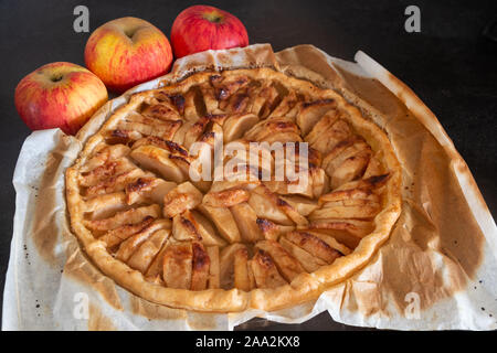 Crostata di mele con carta oleata in un piatto da portata e tre mele Foto Stock