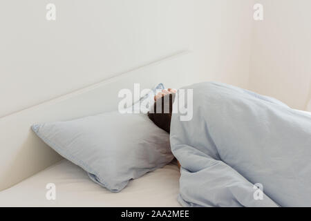 Parte della casa o hotel interior, uomo di dormire su un letto bianco con lenzuola blu al mattino Foto Stock