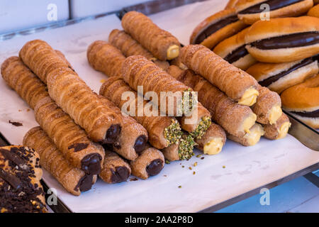 Cannoli torta italiana con pistacchi,panna e cioccolato, close up,dolce italiano su un ripiano un mercato all'aperto.cucina di strada. Foto Stock