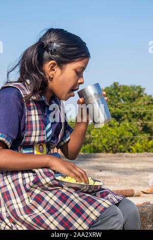 Sijhora,Madhya Pradesh, India- Novembre 19, 2019 : 8 anni piccolo grazioso ragazza indiana di bere acqua dal vetro del tetto. Foto Stock