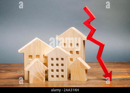 Miniatura case di legno e una freccia rossa verso il basso. Il concetto di basso costo immobiliare. Abbassare i tassi d'interesse ipotecari. Il calo dei prezzi per il noleggio di un alloggiamento Foto Stock