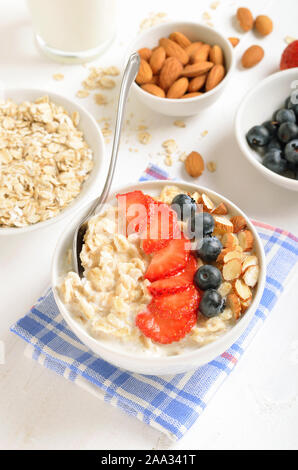 Farina di avena porridge con fette di fragole, mirtilli e i dadi nella ciotola sul tavolo bianco. Mirtilli freschi nella ciotola. Una gustosa prima colazione Foto Stock