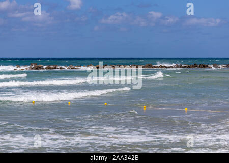 La costa mediterranea vicino a Haifa in Israele, con le onde che si infrangono sulla scogliera di pietra, boe di giallo e blu cielo Foto Stock