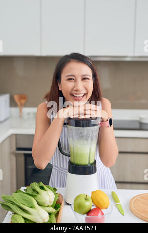 Vegano sorridente donna asiatica facendo un frullato con frutta e verdura in cucina