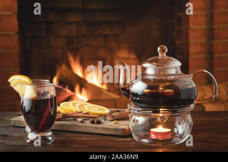 Due bicchieri di vino brulé e teiera su un tavolo di legno davanti a un caminetto a. Foto Stock