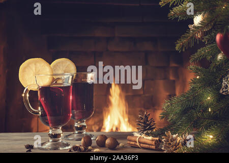 Due bicchieri di vino brulé su un tavolo di legno vicino a un albero di Natale davanti ad un caminetto a. Foto Stock