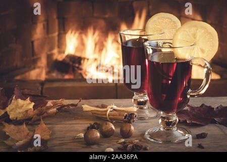 Due bicchieri di vino brulé su un tavolo di legno davanti a un caminetto a. Foto Stock