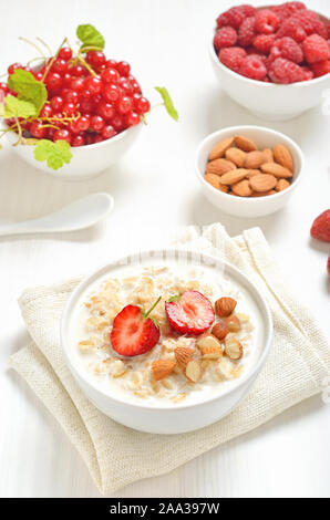 Farina di avena porridge con fette di fragola e i dadi nella ciotola sul tavolo bianco Foto Stock