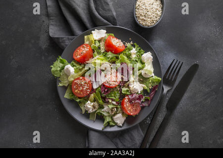Sana insalata vegana in nero il piatto con il pomodoro fresco, verdi, i semi della canapa per pulire mangiare sul nero. Vista dall'alto. Foto Stock