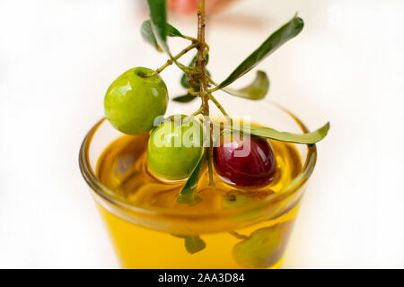 Piccola ciotola di vetro con olio di oliva e decorate con un rametto con olive, frutta isolato su sfondo bianco Foto Stock