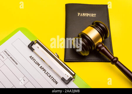 Il concetto di asilo che mostra un modulo per la domanda di asilo su uno sfondo giallo con un martello e un passaporto Foto Stock