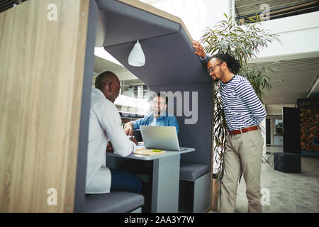 Diversi gruppi di imprenditori sorridente a lavorare insieme su un progetto in una riunione pod nella lobby di un ufficio moderno Foto Stock