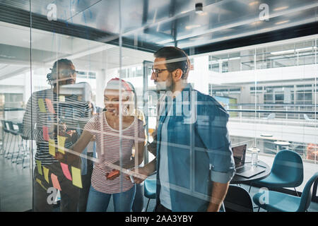 Gruppo di diversi imprenditori utilizzando sticky notes durante una sessione di brainstorming sulla parete di vetro di una sala riunioni in un ufficio Foto Stock