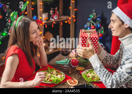 Un uomo è in possesso di una scatola regalo per la sua amata. Un giovane bella coppia di amanti trascorrere una cena di gala nelle decorazioni di Natale Foto Stock