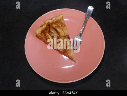 Pezzo di crostata di mele con panna montata e una forcella su una piastra di rosa Foto Stock