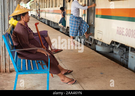 Un anziano di birmani donna vestita di un tradizionale asiatica conica hat e tenendo una canna attende a bordo di un treno a Yangon la stazione centrale Foto Stock