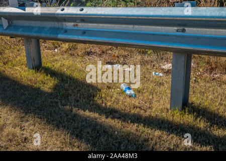 Le bottiglie di plastica di carte e involucri alimentari oggetto di pratiche di dumping sul terreno lungo la superstrada sotto il guardrail in una giornata di sole in autunno Foto Stock