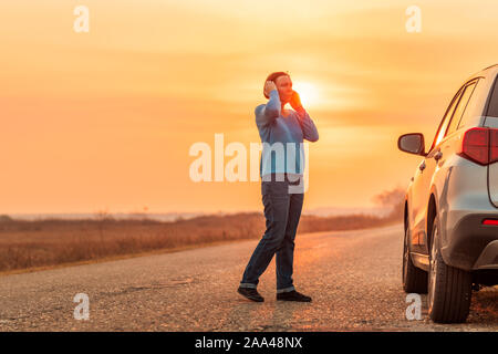 Donna che chiama sul telefono cellulare per ricevere assistenza e aiuto sulla strada dopo la sua auto si è rotta in autunno tramonto sulla strada attraverso la campagna, selettivo foc Foto Stock