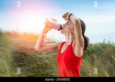 Donna di bere da una bottiglia di acqua mentre exercicing fuori nel sole Foto Stock