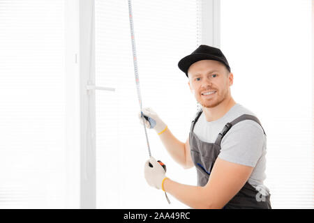 Lavoratore Master guardando la fotocamera e sorridente upvc misure finestra con righello, il processo di installazione. Foto Stock