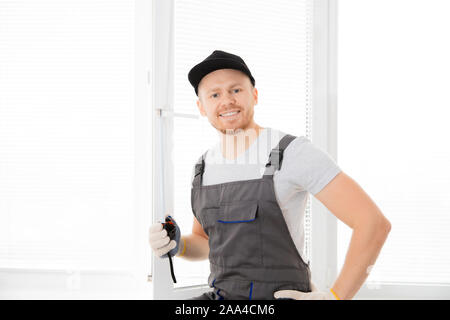 Lavoratore Master guardando la fotocamera e sorridente upvc misure finestra con righello, il processo di installazione. Foto Stock