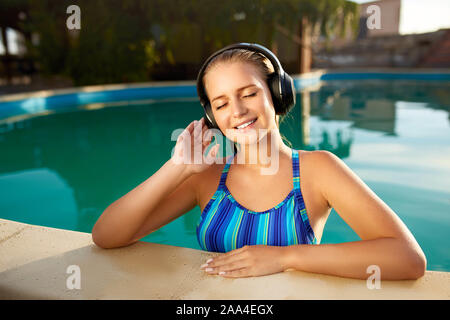 Rilassata donna sorridente ascoltando musica in cuffia la balneazione in  piscina. Ragazza bionda gode di canzone preferita con piccoli brividi sulla  pelle. Impermeabile Foto stock - Alamy