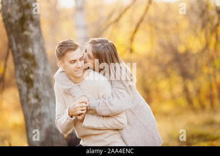 Amare giovane in autunno park con foglie di acero, ragazza sussurra a bella uomo orecchio dichiarazione d'amore. Foto Stock