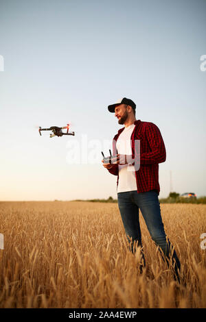 Agricoltore detiene remote controller con le sue mani mentre quadcopter è volare su sfondo. Drone vola dietro l'agronomo nel campo di grano Foto Stock