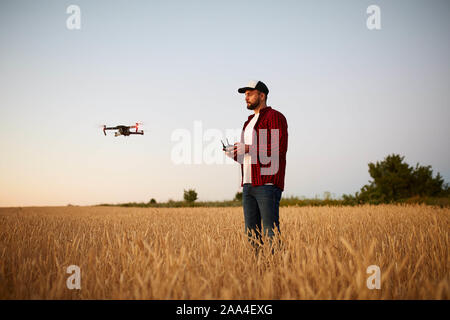 Agricoltore detiene remote controller con le sue mani mentre quadcopter è volare su sfondo. Drone vola dietro l'agronomo nel campo di grano Foto Stock