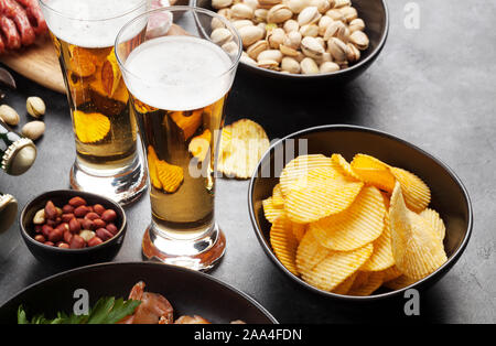 Progetto di birra e spuntini su sfondo di pietra. Dadi, patatine fritte, salsicce e gamberetti Foto Stock