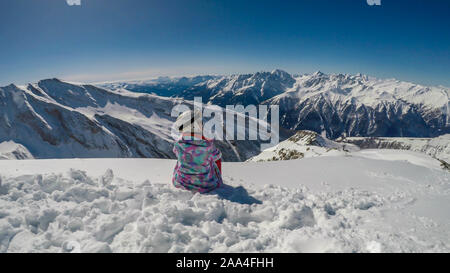 Uno snowboarder ragazza prendendo una pausa sul pendio. Lo snowboard è bianco e blu, armoniosamente il raccordo per la natura condizioni, il bianco della neve, cielo blu. Foto Stock