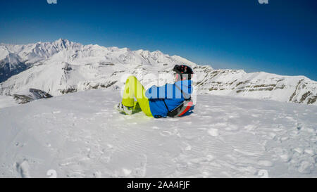 Un giovane uomo è vestito di sci si prende una pausa e giace sulla neve spessa. Egli sta godendo la vista di fronte a lui - Alte Alpi austriache, coperte di neve Foto Stock