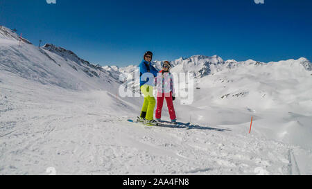 Un paio di sci outfits permanente sulla cima di una montagna innevata e godersi la giornata di sole. Entrambi sono ridendo e godendo della vista. Tall Foto Stock