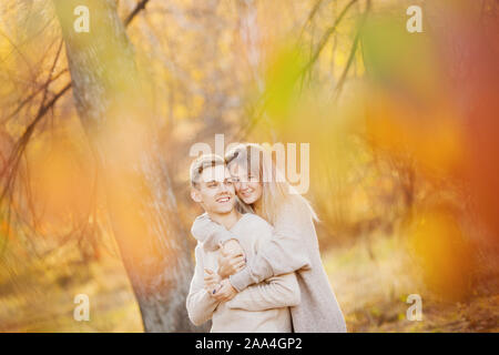 Amare giovane in autunno park con foglie di acero, ragazza sussurra a bella uomo orecchio dichiarazione d'amore. Foto Stock