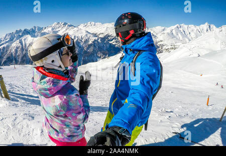 Un paio di sci outfits permanente sulla cima di una montagna innevata e godersi la giornata di sole. Entrambi sono ridendo e godendo della vista. Tall Foto Stock