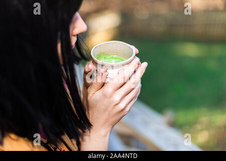 Donna ragazza closeup laterale con nero capelli asiatici holding tazza da tè bere fuori in giardino nel cortile Verde matcha drink a base di erbe Foto Stock