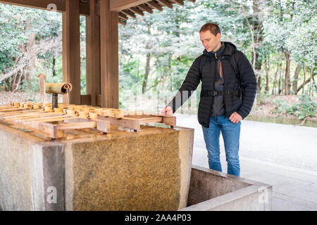 Tokyo, Giappone Meiji con architettura giovane turista uomo con fontana di purificazione siviera lavaggio delle mani Foto Stock